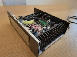 Otwarta obudowa urządzenia audio z transformatorem toroidalnym, płytkami PCB i dużym radiatorem na stole