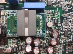 Fragment płytki drukowanej z widocznymi elementami elektronicznymi, kondensatorami i cewką.