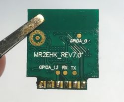 Green PCB labeled MR2EHK_REV7.0, GPIOA_13, RX, TX, held by metal tweezers