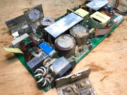Wnętrze zasilacza zasilającego ze śladami korozji i zabrudzeń po zalaniu, przedstawiające elementy elektroniczne na płytce drukowanej.