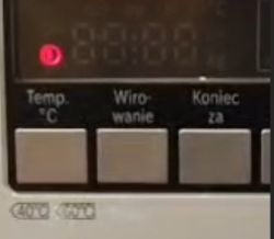 Panel sterowania pralki z pulsującą na czerwono ikoną.