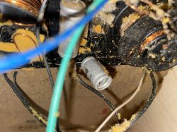 Zbliżenie na wnętrze urządzenia elektronicznego z widocznymi elementami, takimi jak kondensatory i kable.
