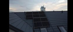 Panele fotowoltaiczne na dachówce z kominem i anteną satelitarną w tle