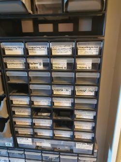 Organizer z plastikowymi szufladkami na części elektroniczne, z opisami etykietami.