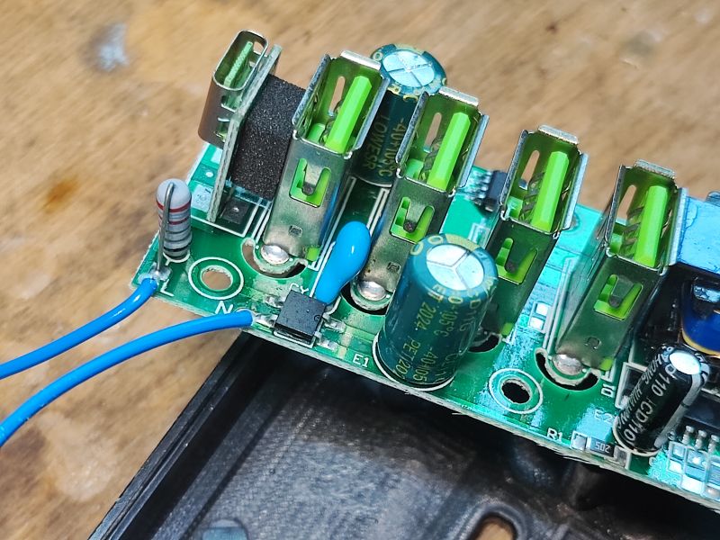 Zbliżenie na płytkę PCB z czterema portami USB typu A, kondensatorami elektrolitycznymi i przewodami niebieskimi podłączonymi do gniazd.