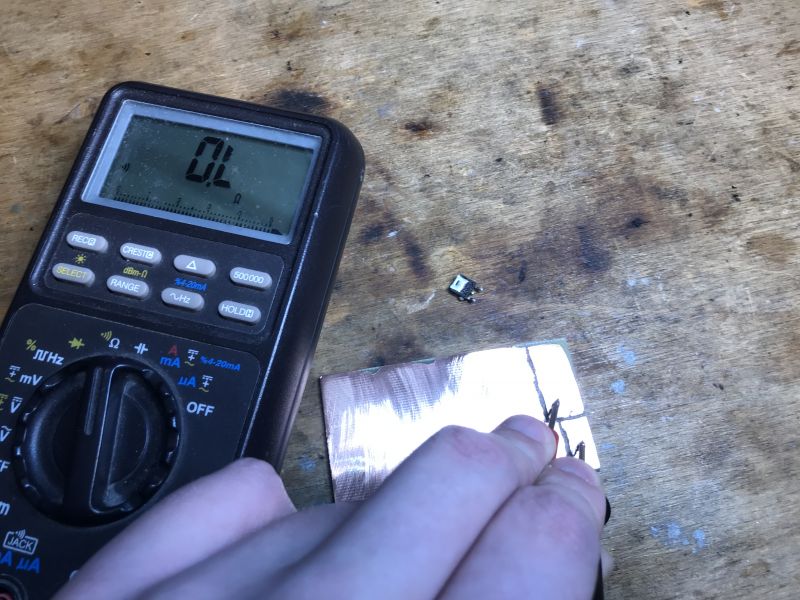 Multimeter and Transistor on Copper Laminate Multimeter on a wooden table next to a copper laminate and a transistor.