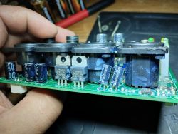 Zbliżenie na płytkę PCB z widocznymi elementami elektronicznymi, w tym kondensatorami i tranzystorami L7812CV, trzymaną w ręce.