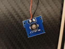 Niebieska płytka drukowana z uszkodzonym przyciskiem i gumeczką na tle włókna węglowego.