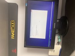 Ekran monitora Samsung podczas instalacji systemu Windows, obok naklejka z napisem FAKETAXI.