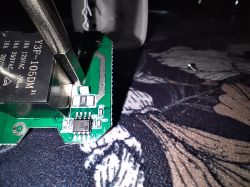 Close-up of a circuit board with a Y3F-105DM relay and the tip of metal pliers.