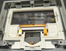 Wnętrze miernika z miedzianą dźwignią blokady wskazówki i napisem „Zaaretowane, blokada podniesiona”