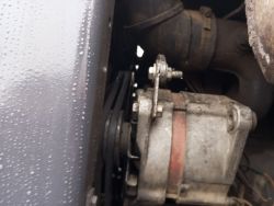 Alternator pojazdu z widocznymi paskami napędowymi i wilgocią na metalowej powierzchni.
