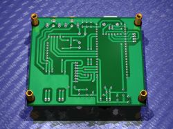 Bottom view of green PCB showing traces, pinholes, and four metal standoffs in corners