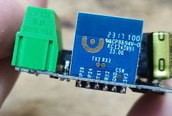 Close-up of a blue PCB with a green screw terminal block and visible silkscreen showing pins.