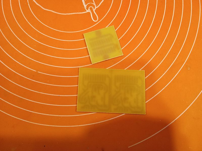 Two yellow PCB pieces on an orange mat with concentric circles.