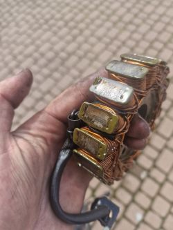 Ręka trzyma zużyty stator z motocykla, widoczne starcia na magnesach.