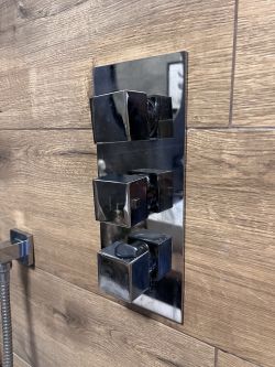 Omnires Fresh concealed shower set with three metal knobs mounted on wood-like tiles.