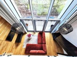Top view of a living room with large windows, a red corner sofa, and wooden flooring.