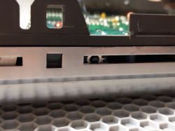 Fragment urządzenia elektronicznego z obudową i widoczną płytą drukowaną w tle.