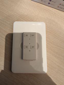 Remote for Prime WiFi Outdoor Outlet from Costco White remote with four buttons: two ON and two OFF, placed on a white stand on a wooden table.
