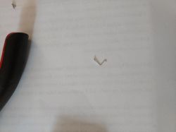 Small, bent wire on a white surface next to a black handle tool.