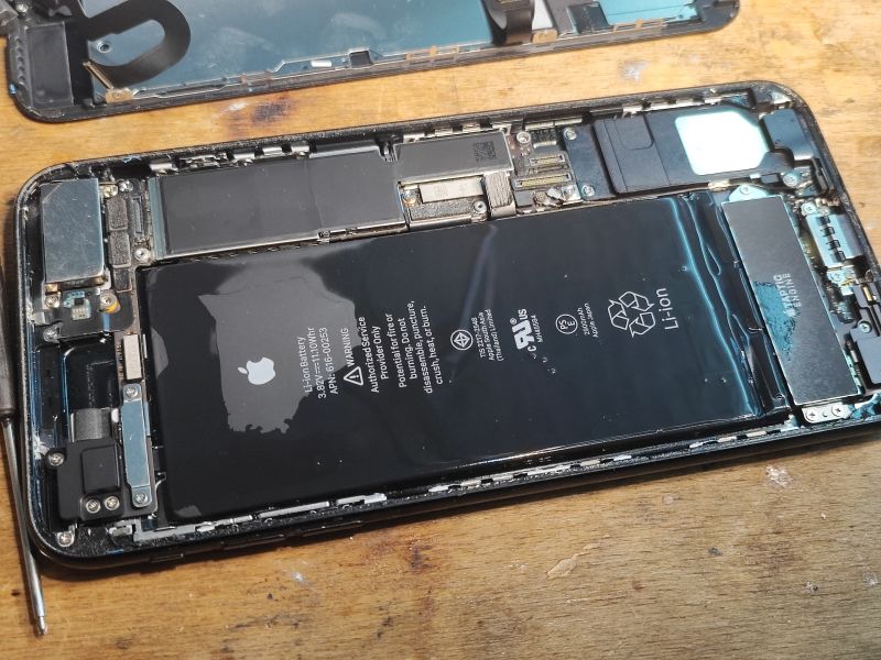 Step-by-Step iPhone Battery Replacement Disassembled iPhone with exposed battery on a table.