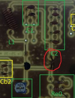 Zbliżenie na płytkę drukowaną z różnymi elementami elektronicznymi, w tym cewką i identyfikowanymi ręcznie kondensatorami.