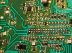 Zbliżenie na płytkę drukowaną z widocznymi lutami i komponentami elektronicznymi.