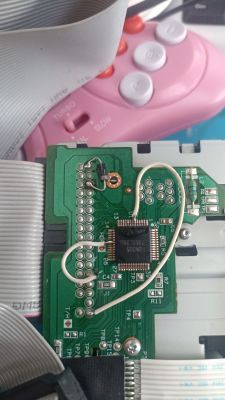 Modified NEC FD1231H floppy disk connected to a circuit board with visible wires and a chip. A pink controller is in the background.
