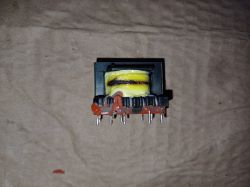 Transformator elektroniczny z żółtym uzwojeniem na tle brązowego papieru.