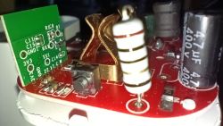 Close-up of an electronic module with components like resistors, capacitors, and buttons on a red circuit board.