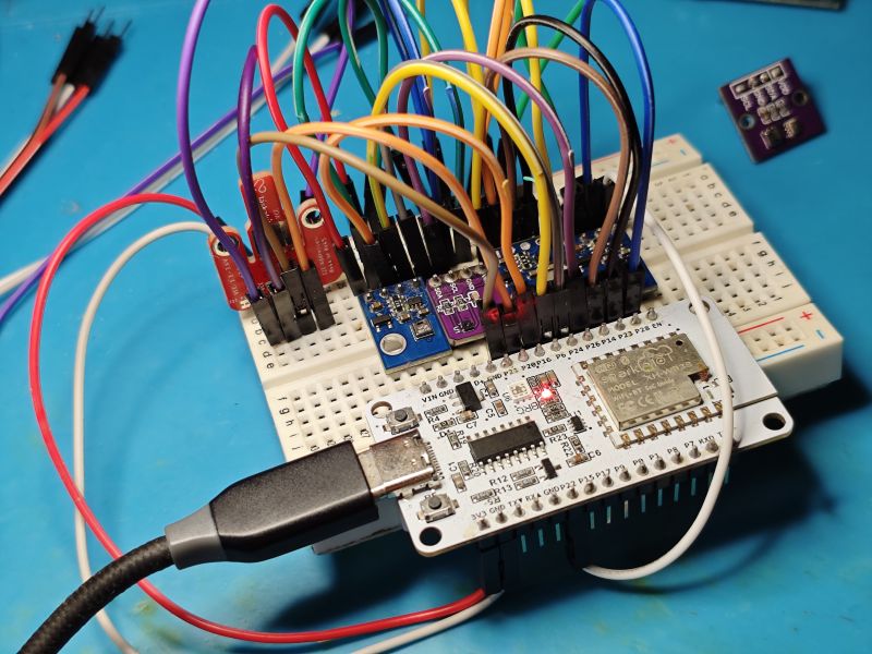 ESP32 board on a breadboard with many jumper wires and a sensor module; USB cable attached on blue mat