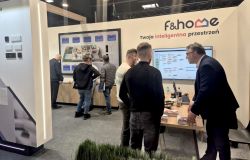 f&amp;home trade show booth with two screens, a table, and people talking