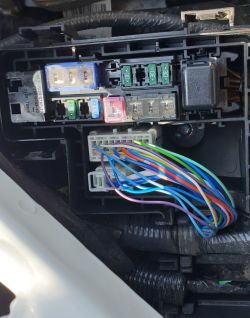 Widok na panel bezpieczników w samochodzie z wielobarwnymi kablami.