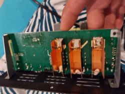 Close-up of a green circuit board with three large copper heatsinks inside electronic equipment.