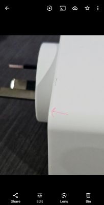Close-up of a white electronic device with visible plug part, arrow pointing to a seam on the casing.