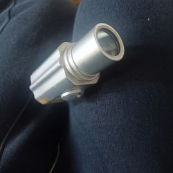 Metalowy obiekt przypominający teleskop na tle ciemnego materiału.