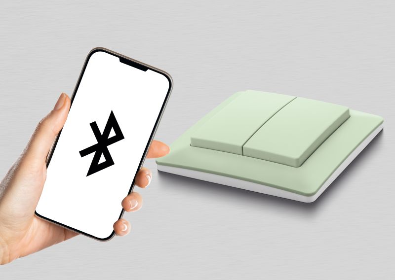 Dłoń trzyma smartfon z ikoną Bluetooth obok zielonego podwójnego włącznika światła