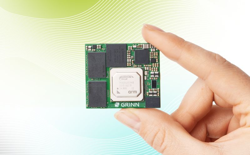 Hand holding a small green GRINN circuit board with an ARM chip in the center.