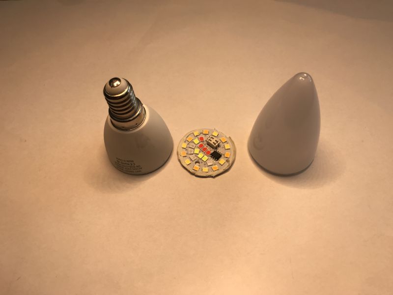 Disassembled WiFi LED Bulb with Exposed LED Board Disassembled LED smart bulb: casing, LED board, and dome cover placed on a light surface.