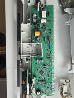 Zbliżenie na zieloną płytę drukowaną z elementami elektronicznymi, umieszczoną w plastikowej obudowie.