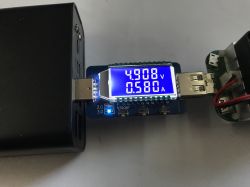 Power bank connected to a USB meter showing 4.908 V and 0.580 A on a white surface
