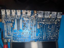 Spód niebieskiej płytki PCB wzmacniacza z wieloma ścieżkami i lutami oraz rzędem elementów mocy u góry