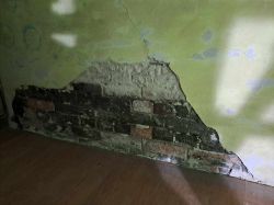 Fragment ściany z widoczną warstwą cegieł, gdzie odpadł tynk.