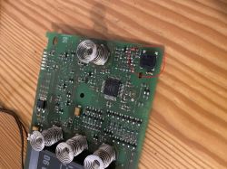 Płytka PCB z zaznaczonym układem scalonym i widocznymi sprężynami na tle drewnianym