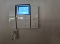 Stary monitor wideo-domofonu Commax podłączony do ściany, z wyświetlonym obrazem z kamery.
