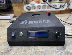 Czarna obudowa urządzenia DUMMYLOAD V2 z LCD, przełącznikiem, przyciskiem i pokrętłem na stole warsztatowym