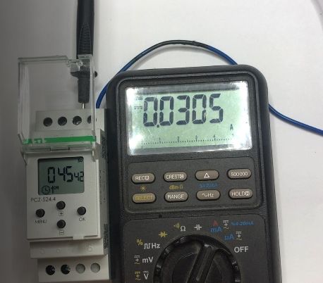 Multimetr cyfrowy pokazujący pomiar prądu obok elektronicznego przekaźnika czasowego.