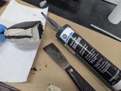 Permatex black silicone and hand tools next to taped object being sealed