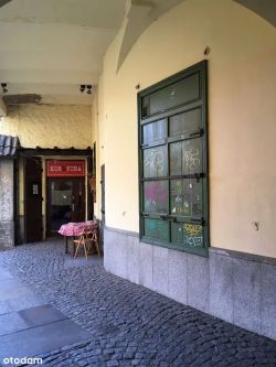 Covered entrance to a restaurant with a Kons Pira sign above the door and a table with chairs outside.
